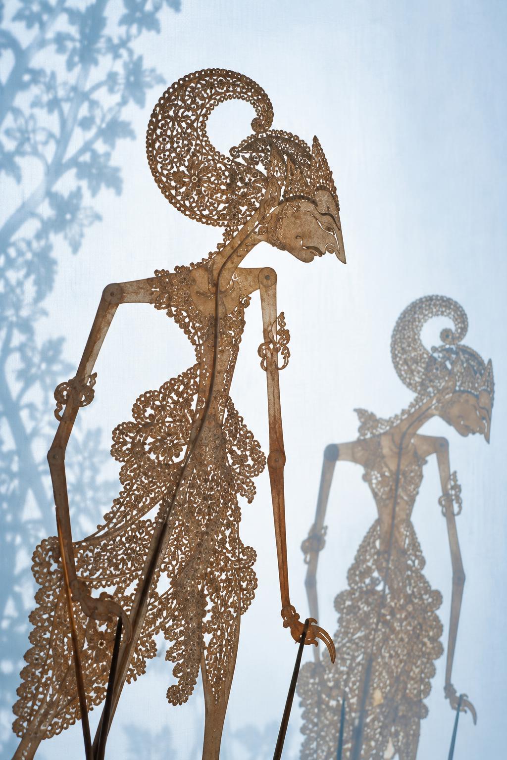 Traditional wayang kulit shadow puppets backlit against a pale screen